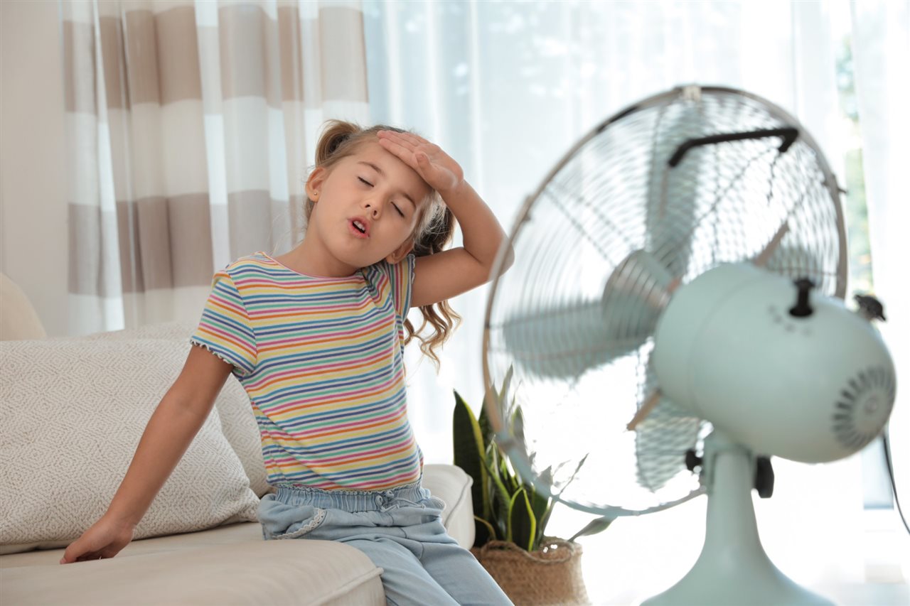 Girl wiping her brow in front of a fan. Stay cool and save with energy-smart solutions at oncourse.com.
