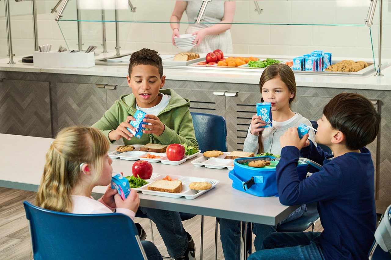 Four children sit at a lunch table, drinking milk with their lunch.