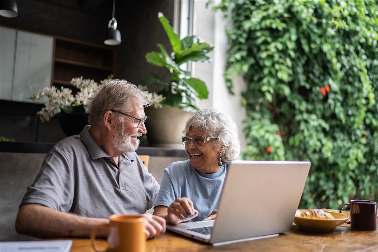 Older couple in a booth in a restaurant with a laptop reviewing their medication options online.